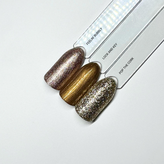 en Vogue Lac it! lock-key antique gold pearl UV/LED gel polish for professional nails and extensions show on a swatch stick with feelin' Bubbly and Pop the Cork swatches for comparison
